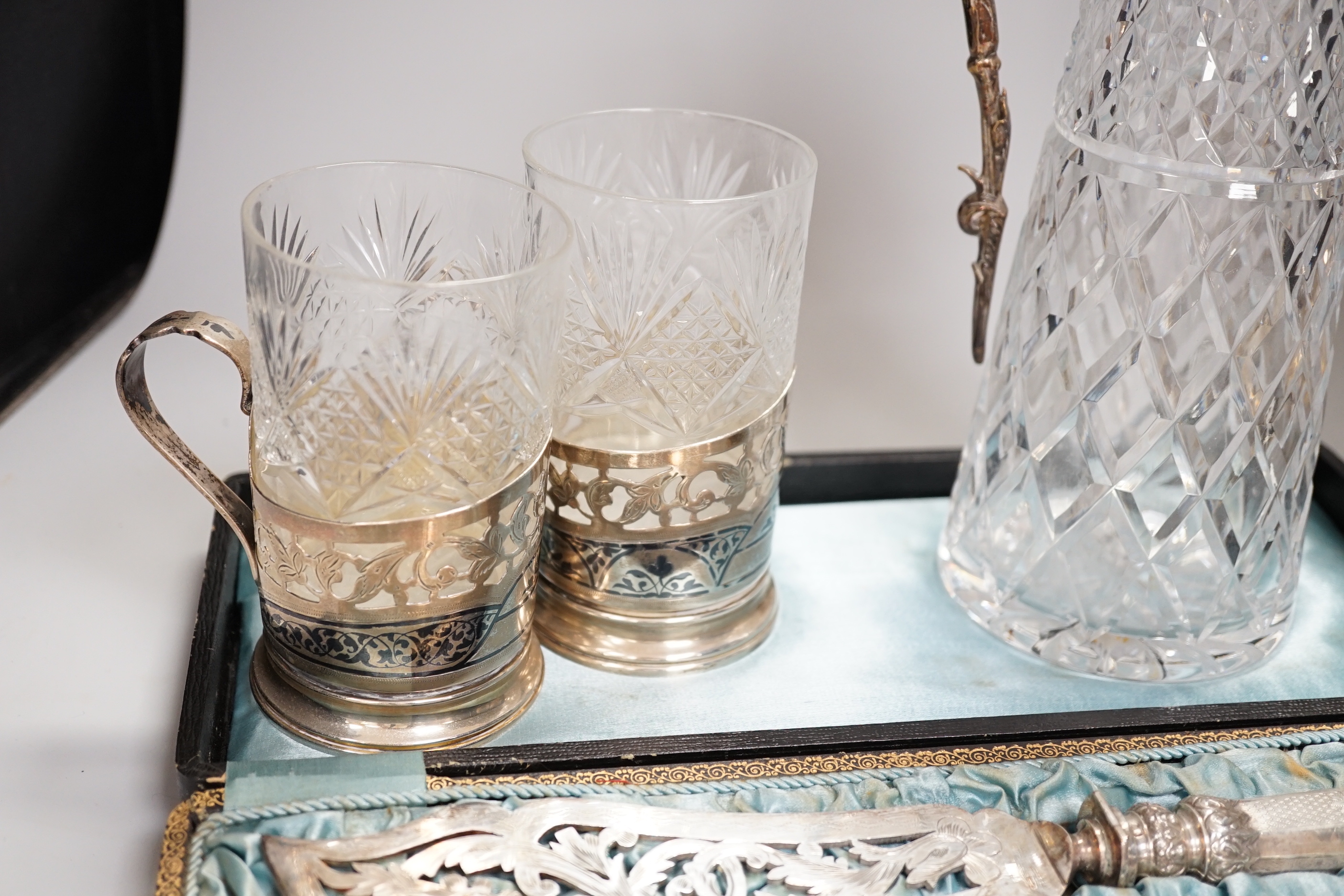 Two claret jugs, one with gilt decoration, four silver plated cup holders with glass liners and silver plated fish servers, the largest 32cm high